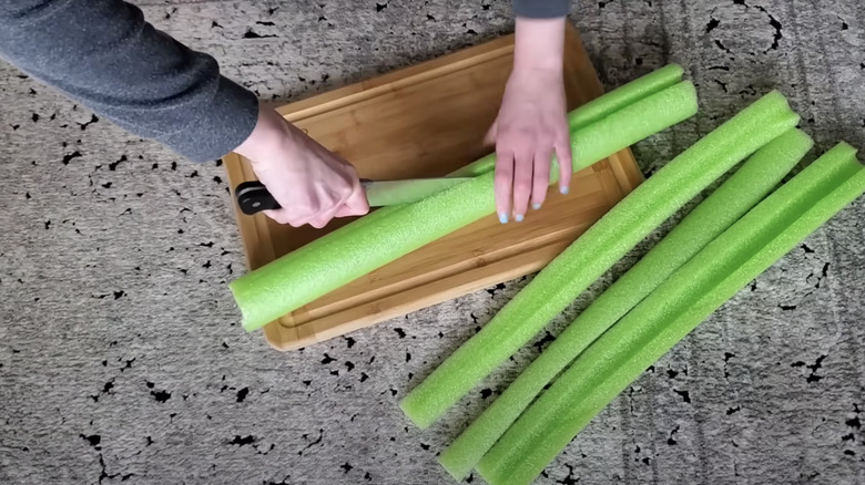 person cutting pool noodles lengthwise on a cutting board